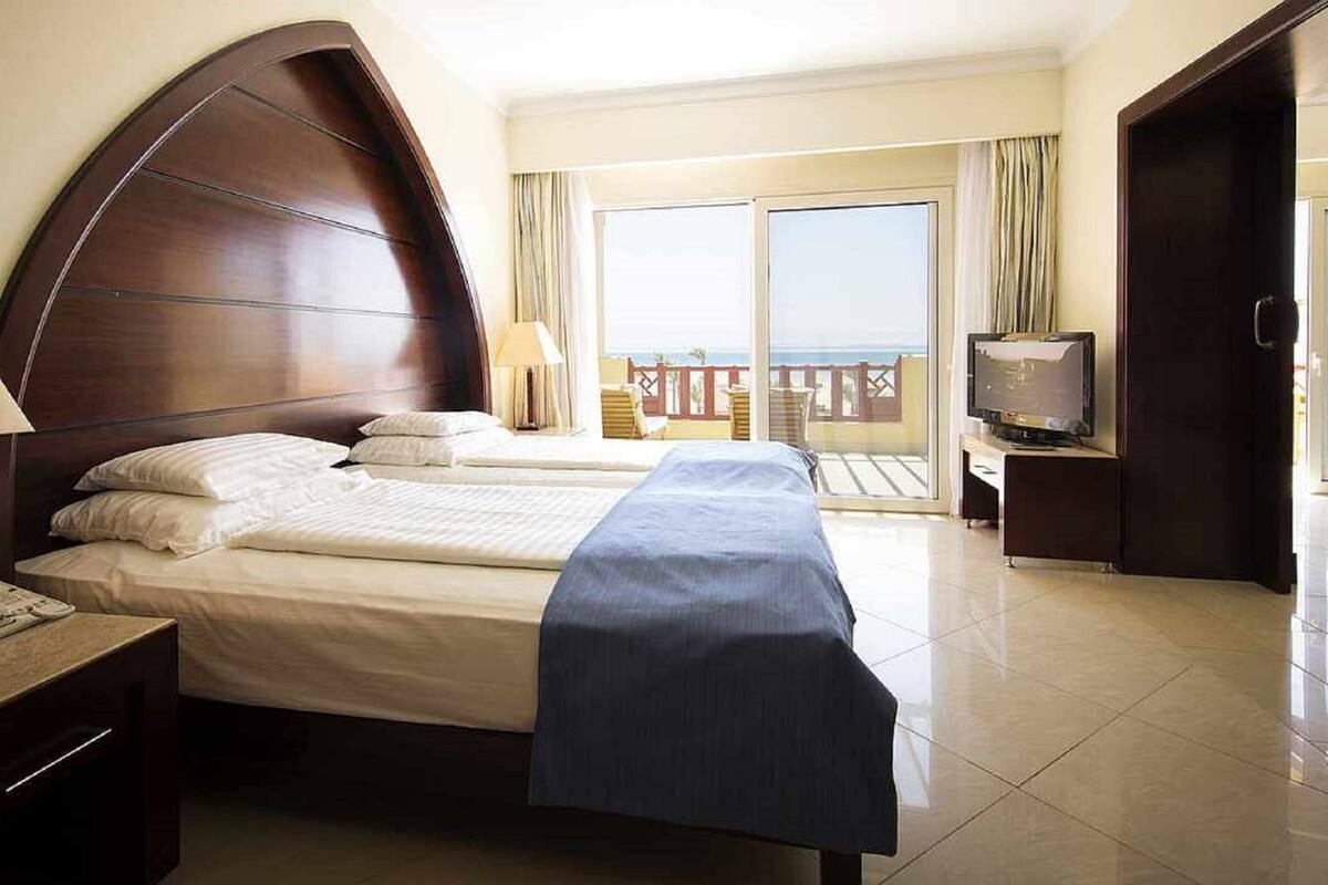 Quarto de hotel com cama grande, televisão e varanda com vista.