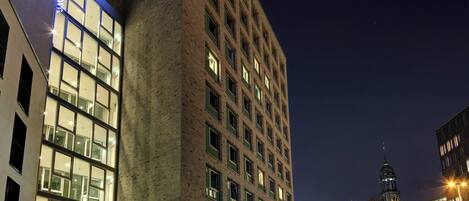 Un hotel moderno con un llamativo letrero de 'Motel One', grandes ventanales y un área de entrada bien iluminada.