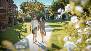 A couple walking on a paved path in a well-maintained garden area with grass and trees. - ROBINSON QUINTA DA RIA - All Inclusive (Vila Real Santo Antonio)