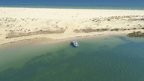 An aerial view of a beach with clear water, a sandy shore, and a boat in the water. - ROBINSON QUINTA DA RIA - All Inclusive (Vila Real Santo Antonio)