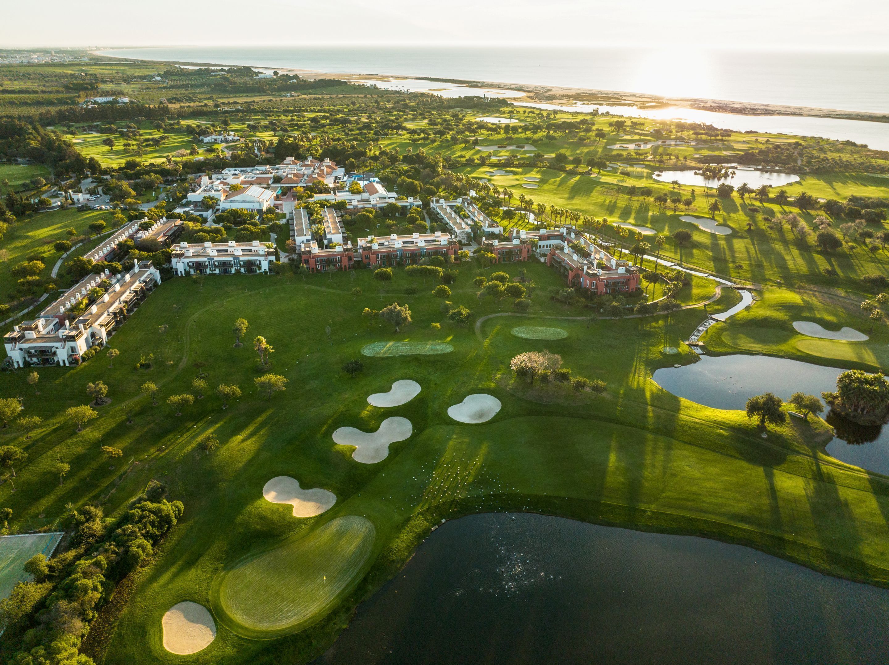 Une vue aérienne d’un terrain de golf avec de nombreux bunkers, un club-house et une grande étendue d’eau.