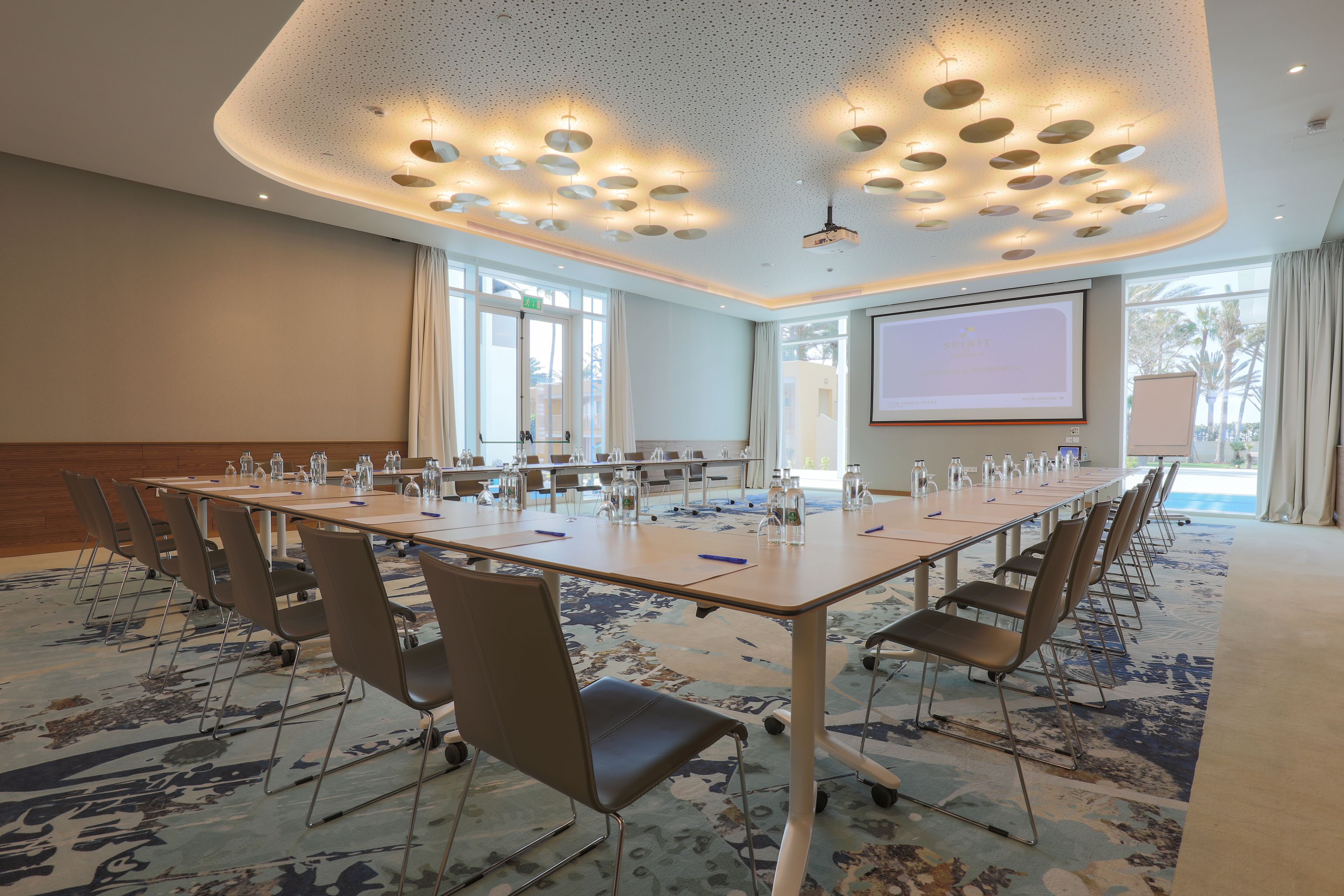 A conference room with a long table, chairs, a projector screen, and a carpeted floor.
