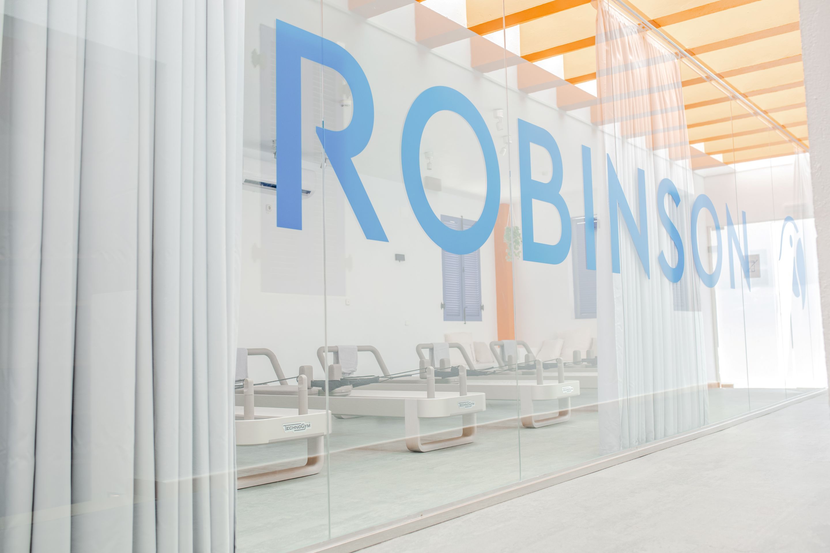 A modern interior with a glass wall displaying the word 'ROBINSON' and a row of exercise equipment.