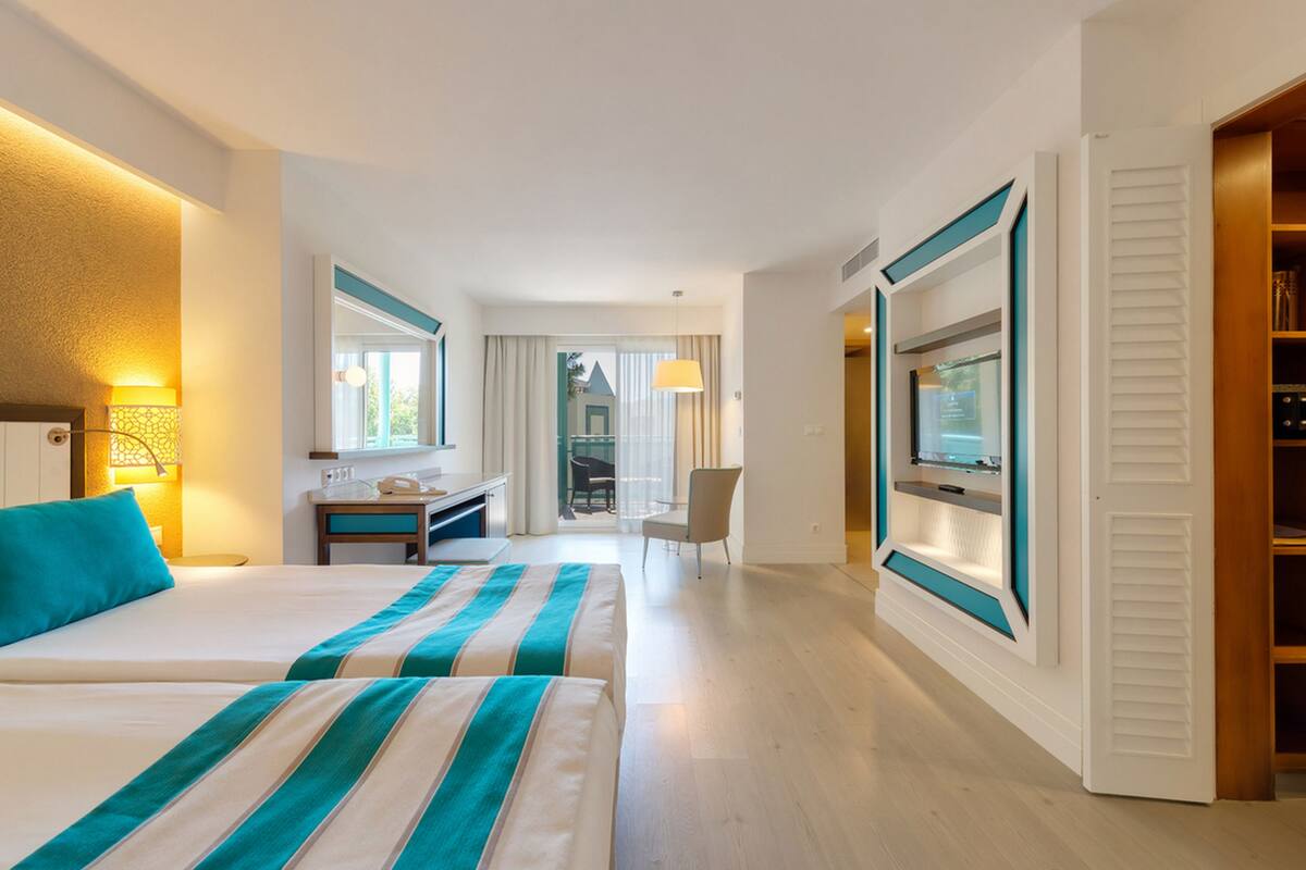 Habitación de hotel con dos camas, un escritorio, una silla, un televisor y vistas al exterior.
