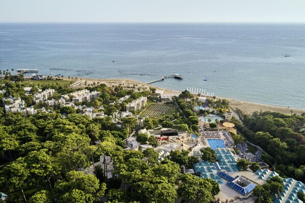 Luftaufnahme eines Küstenresorts mit mehreren Gebäuden, einem Strand und einem Poolbereich.