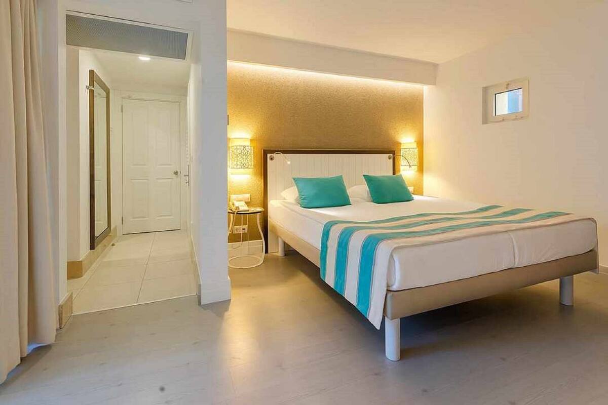 Un dormitorio con cama, mesita de noche y puerta que da a otra habitación.