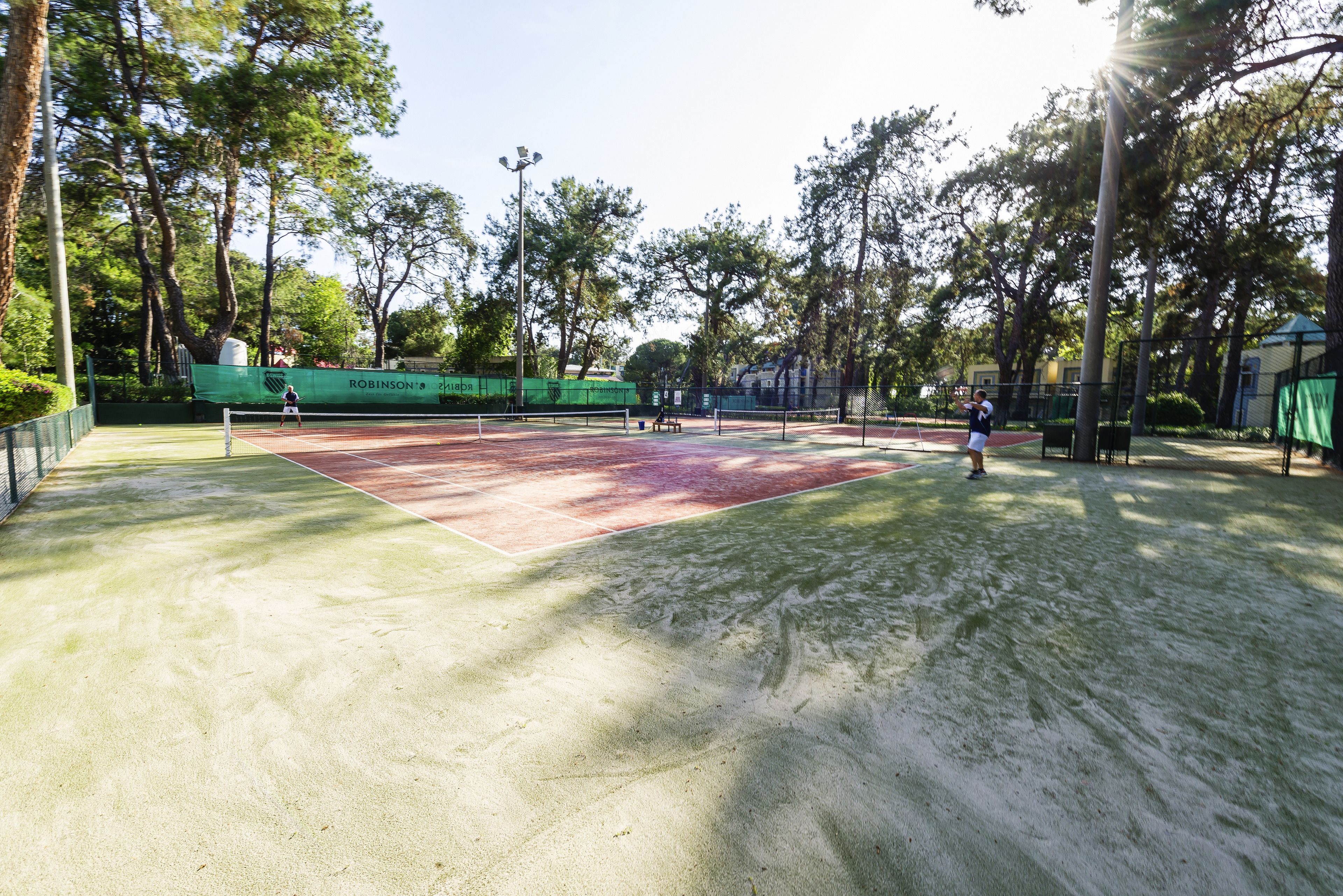 A tennis court with a net, surrounded by trees and a green fence.