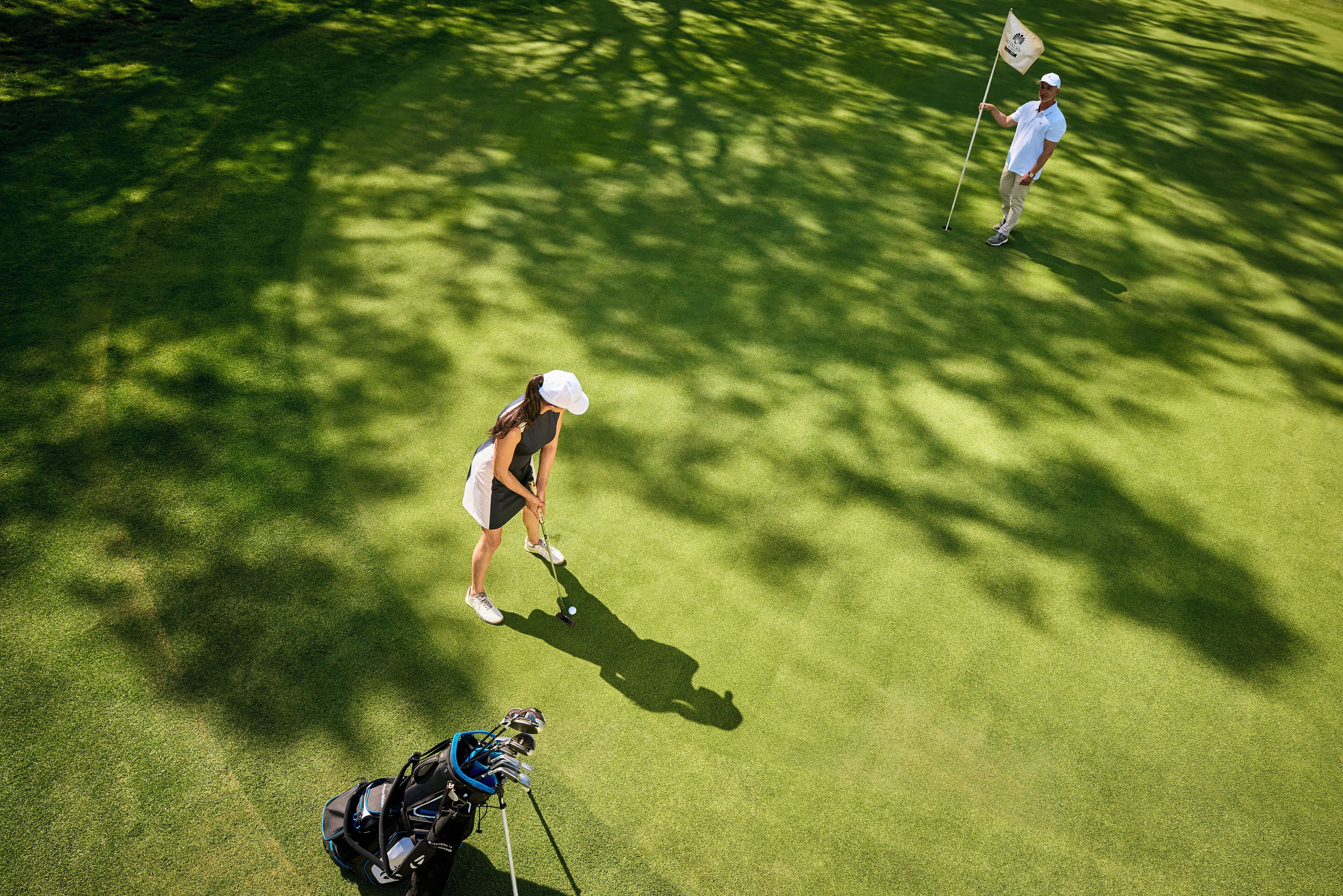 A golf course with a putting green, a flagstick, and a golf bag.