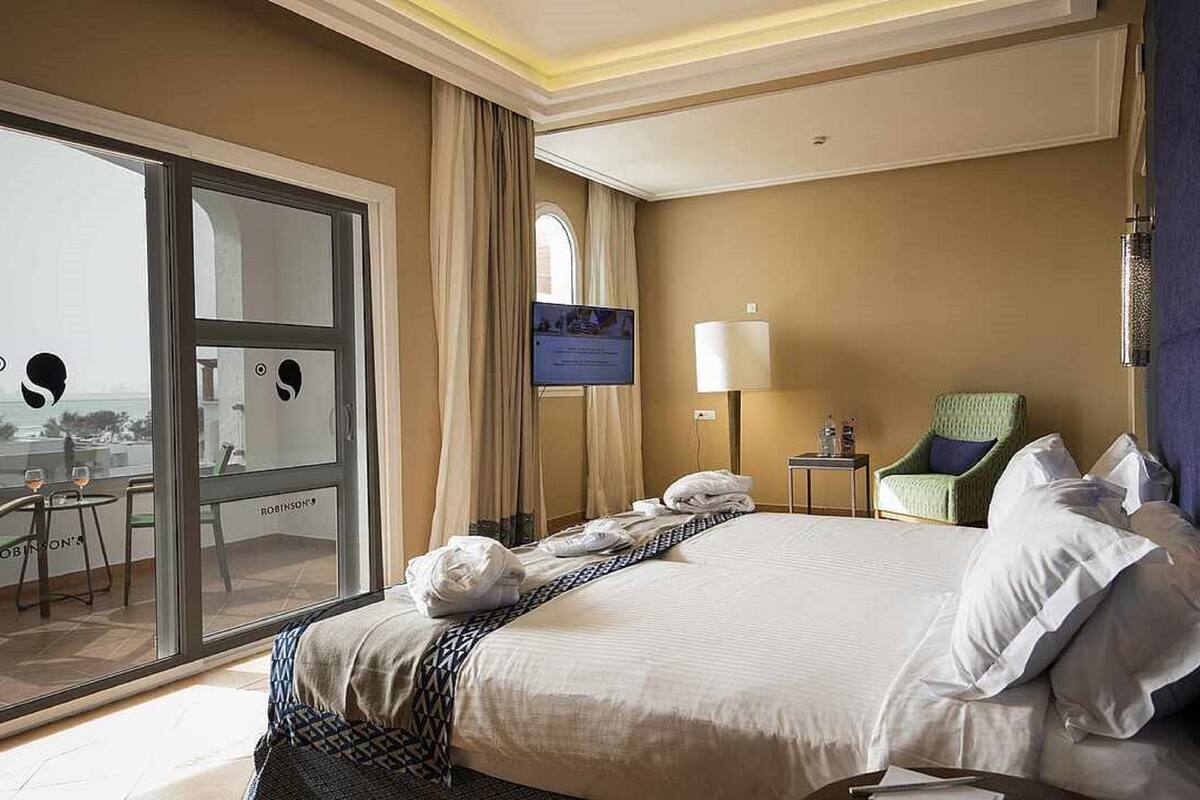 Quarto de hotel com uma cama grande, uma cadeira, uma TV e vista para o oceano através de uma porta de correr.