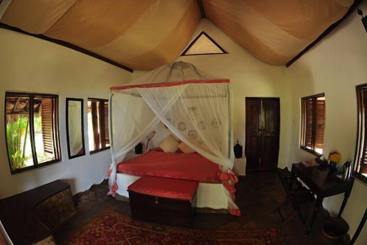 A room with a bed under a canopy, a desk, and a chair.