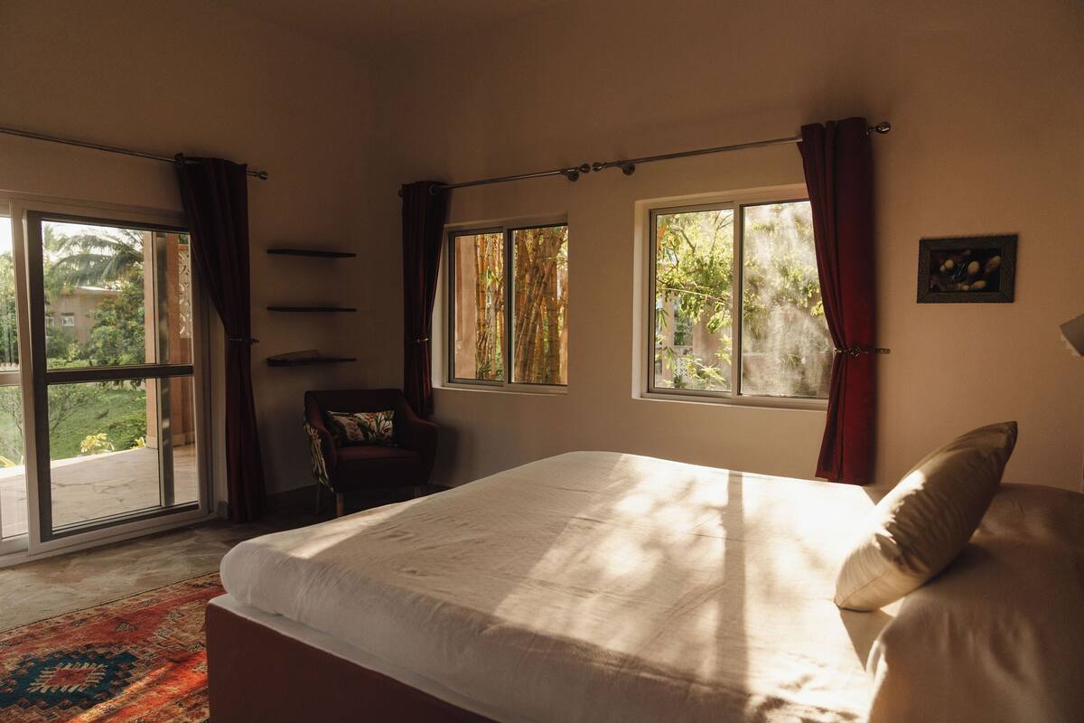 A bedroom with a large bed, a chair, and a window with curtains.