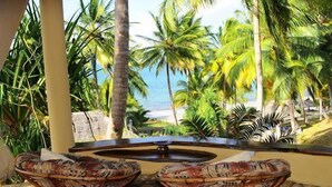 A view from a balcony with two wicker chairs, overlooking a beach with palm trees and the ocean. - Kinasi Lodge (Mafia Island)