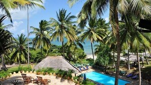 A pool area with lounge chairs, a thatched-roof structure, and palm trees. - Kinasi Lodge (Mafia Island)
