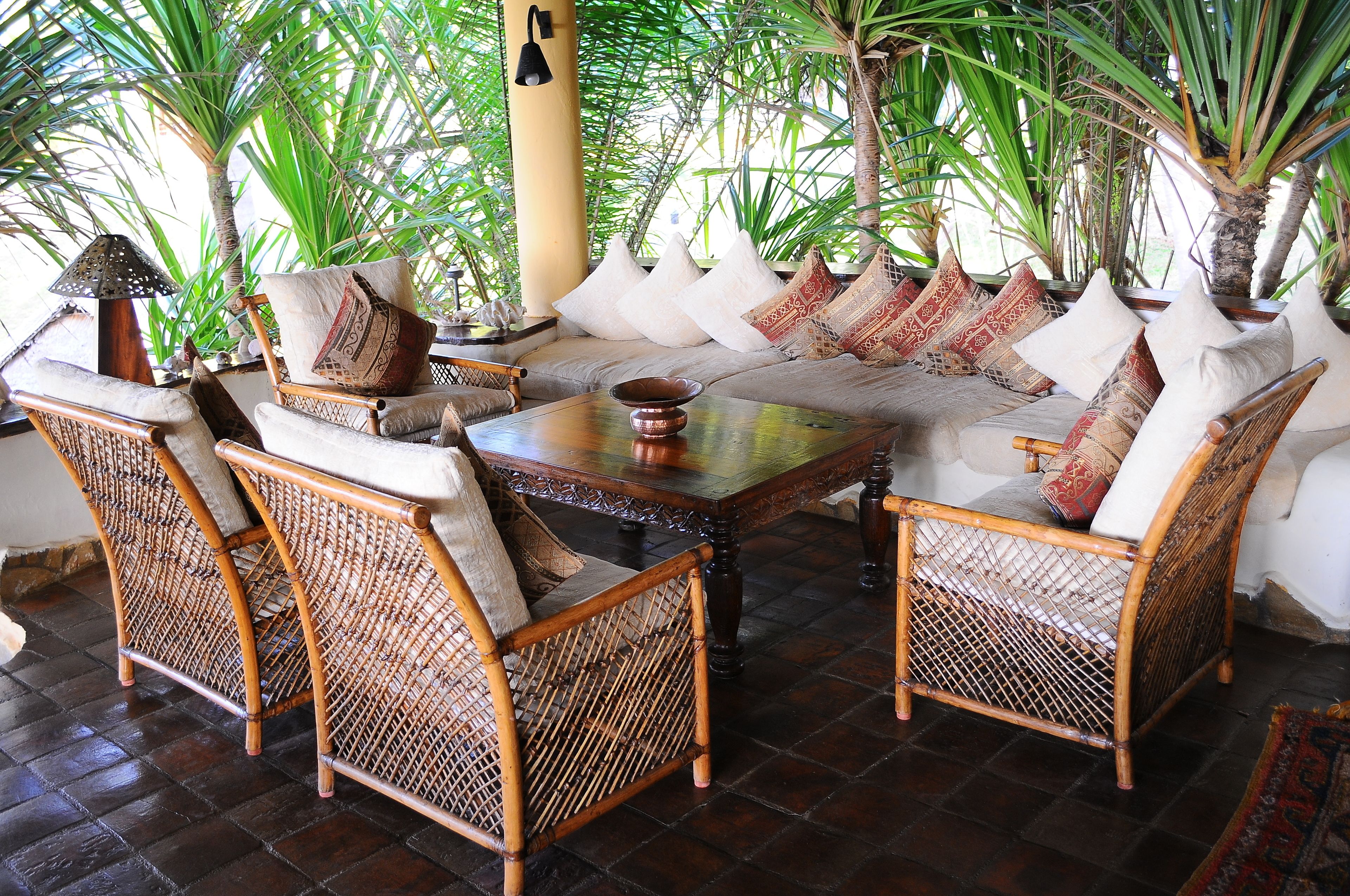 A cozy seating area with wicker furniture and patterned cushions, surrounded by lush green plants.