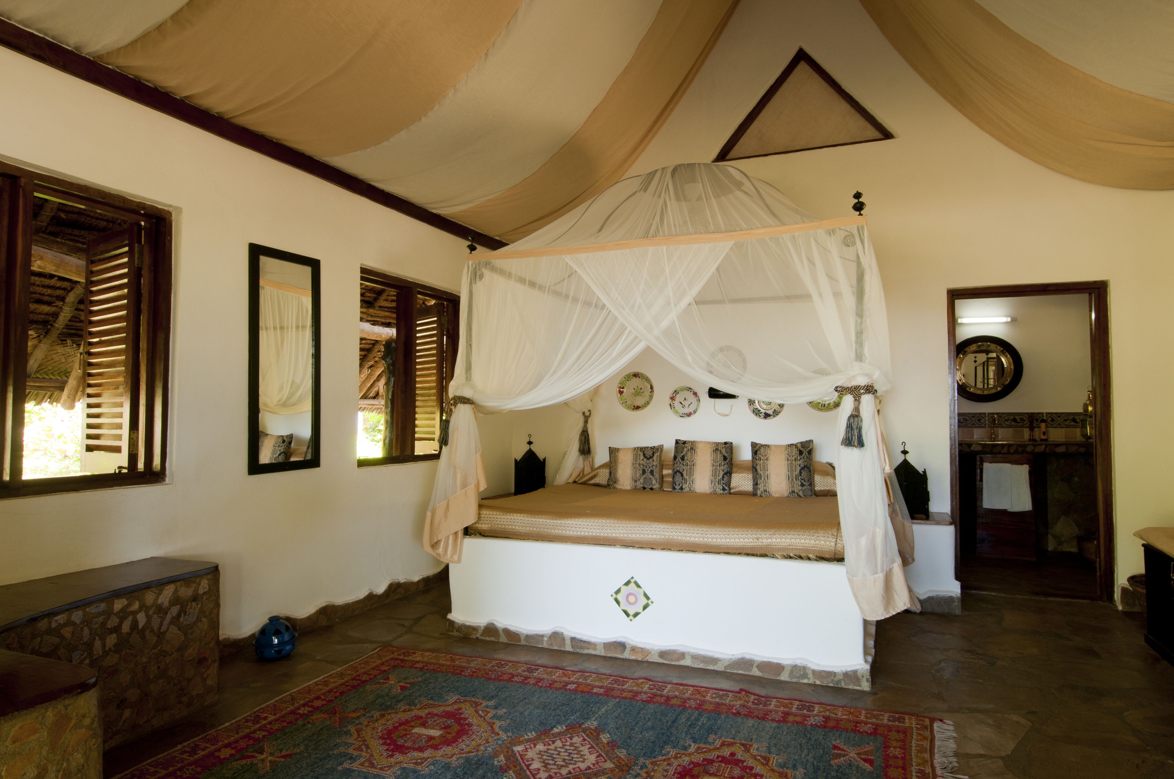A room with a four-poster bed, a stone bench, and a patterned rug.