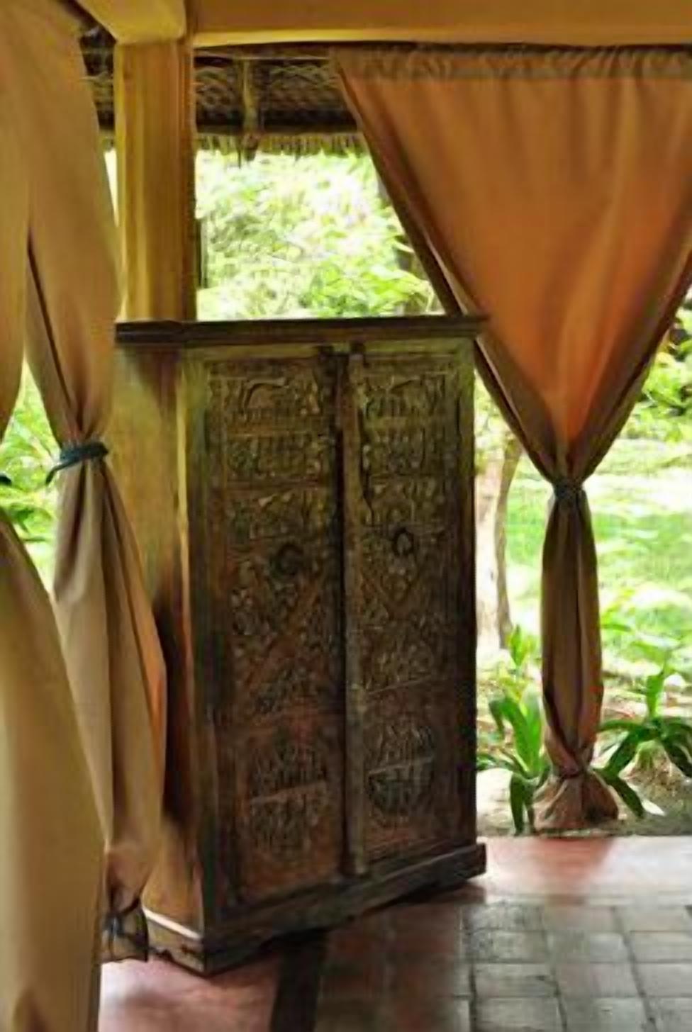 A wooden cabinet with intricate carvings, positioned under a canopy with curtains.