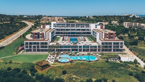 Ein modernes Hotel mit mehreren Schwimmbecken, einem gepflegten Rasen und Blick auf die umliegende Landschaft.