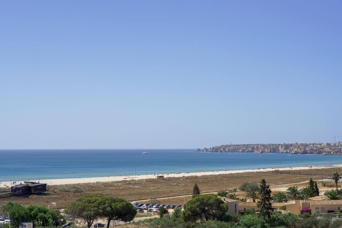 A coastal view with a beach, a parking area, and a distant cityscape.