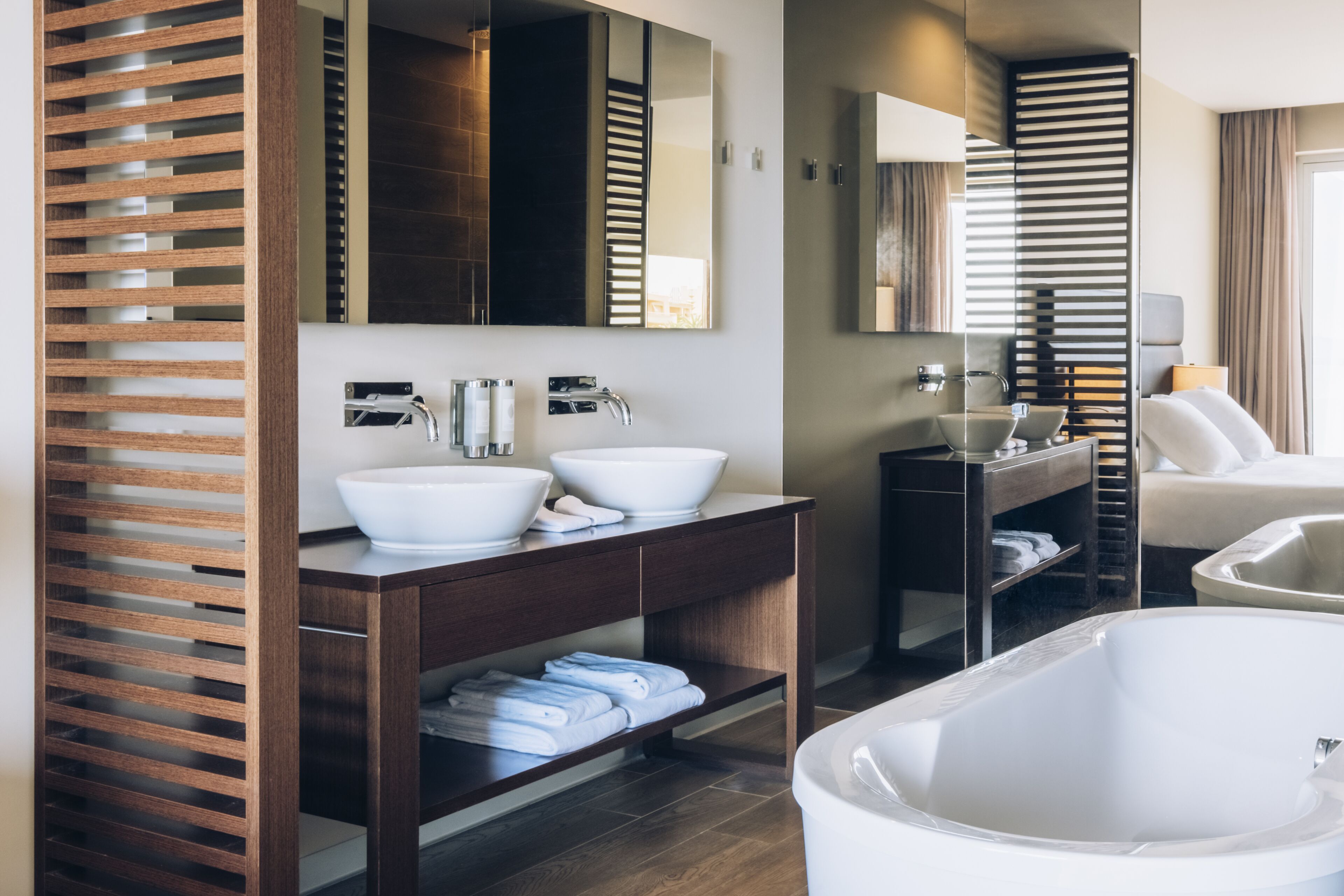 Un baño moderno con dos lavamanos, una bañera grande y estantes de madera con listones.