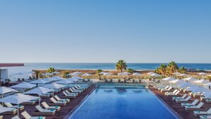 Ein Poolbereich mit Liegestühlen und Sonnenschirmen mit Blick auf Strand und Meer.