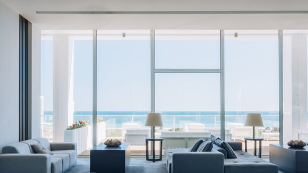 Ein modernes Wohnzimmer mit großem Fenster mit Meerblick, zwei Sofas, einem Couchtisch und einem Beistelltisch mit Lampe.