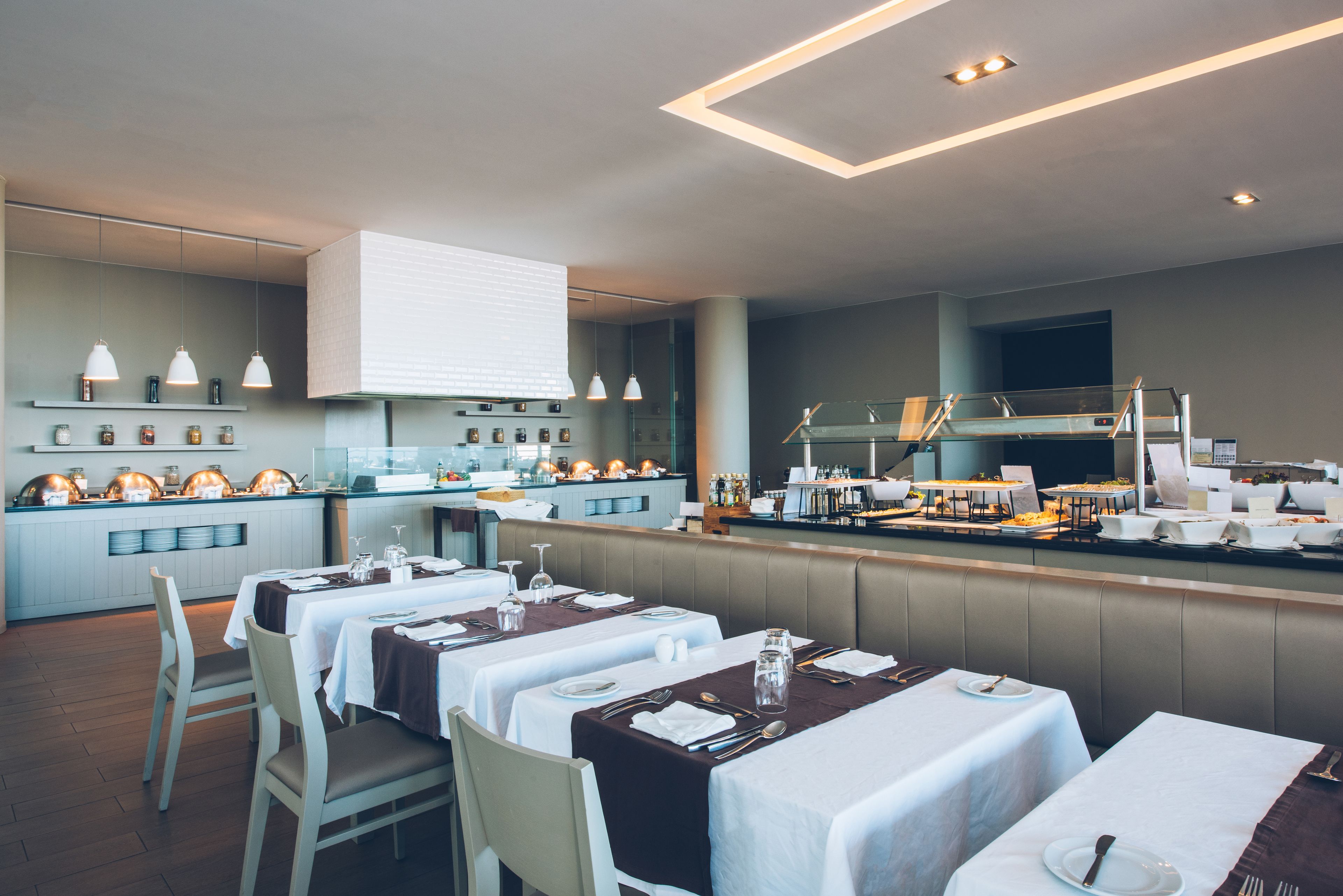 Un restaurante con varias mesas dispuestas para comer, una zona de cocina y un bar.