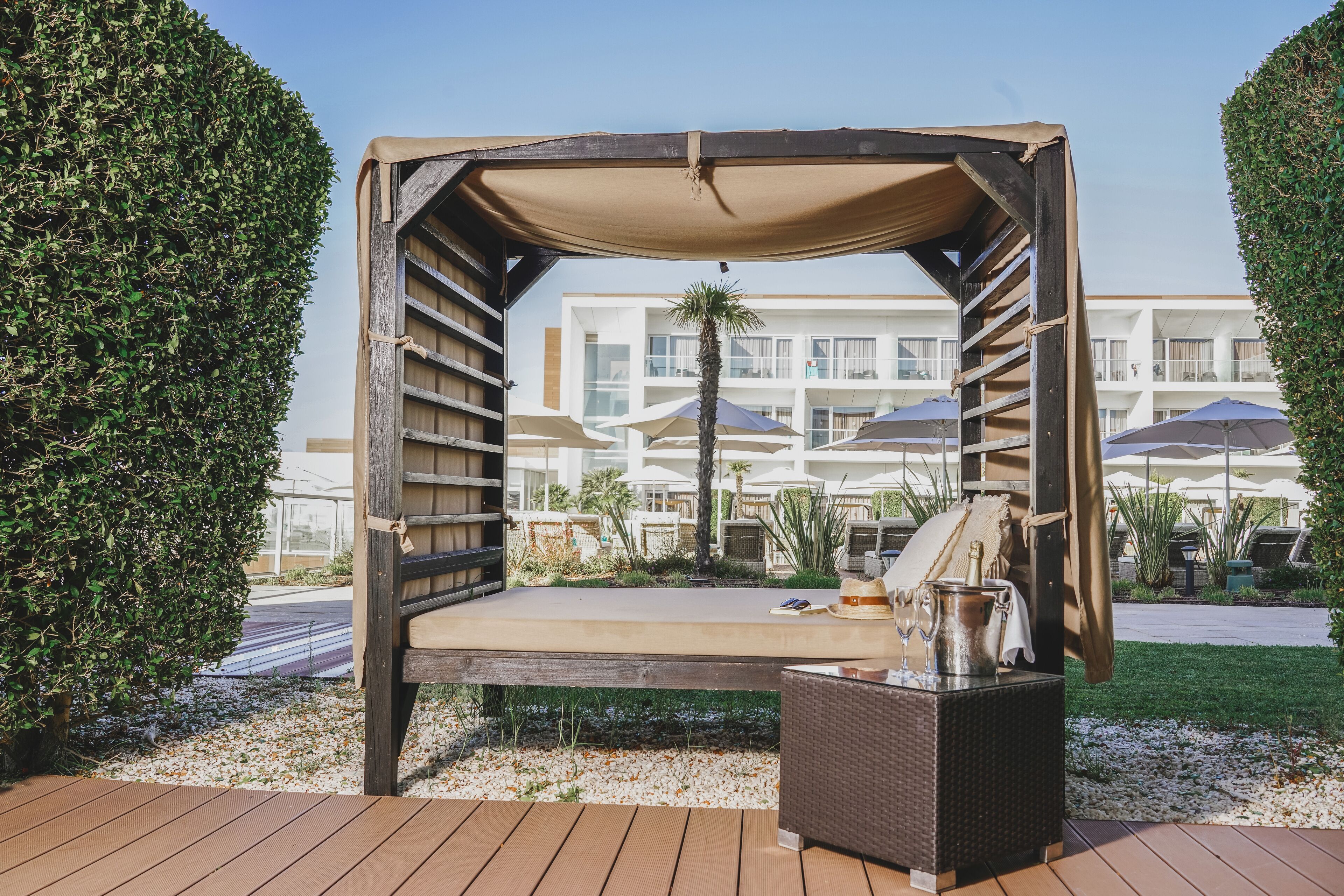 Un espace extérieur abrité, aménagé avec un banc en bois, une table en osier et une bouteille de champagne.