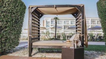 Un espace extérieur abrité, aménagé avec un banc en bois, une table en osier et une bouteille de champagne.