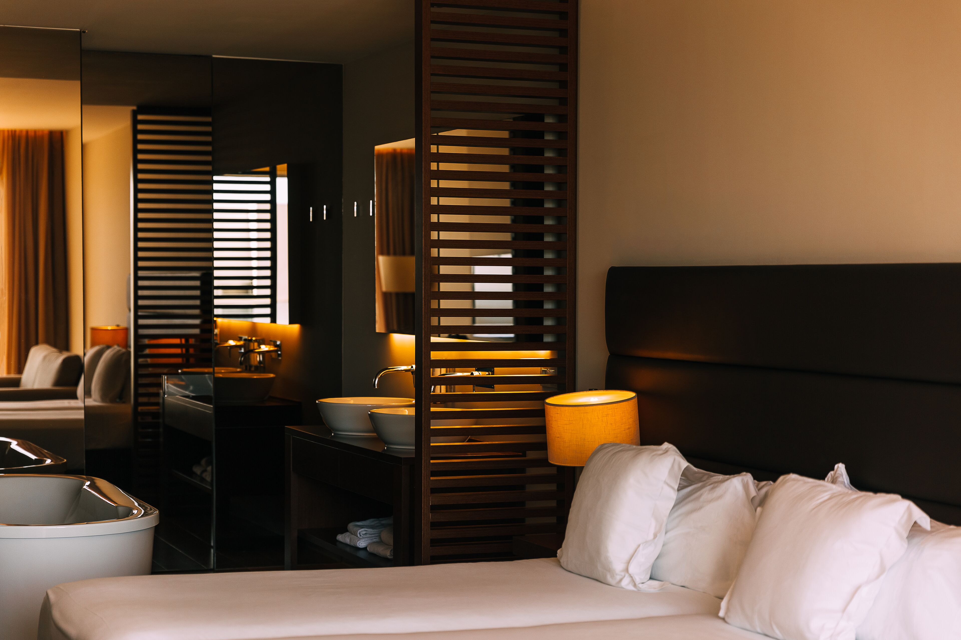 A hotel room with a bed, a bathroom, a sink, and a mirror.