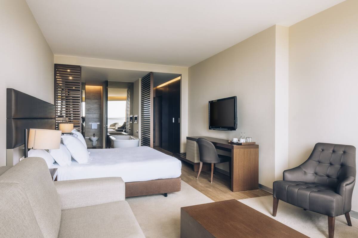 A modern hotel room with a bed, a desk, a chair, a TV, and a sofa.