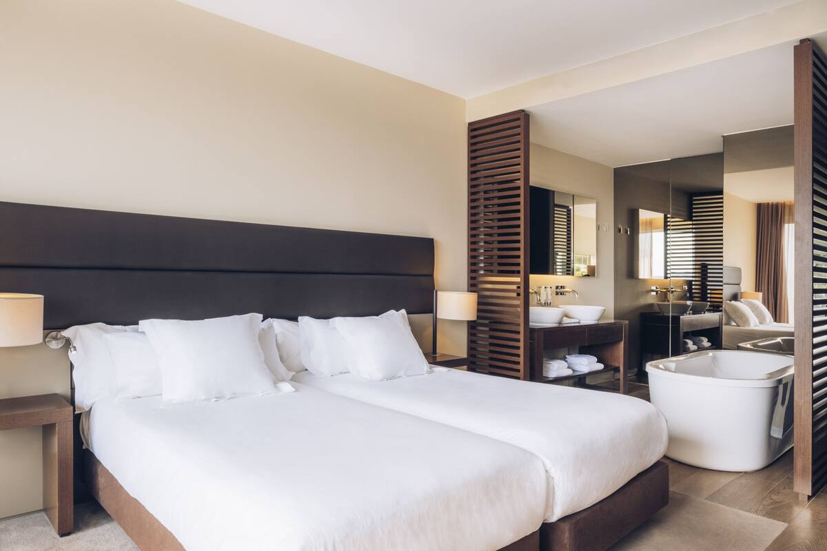 A hotel room with a large bed, a bedside table, a bathroom with a bathtub, and a mirror.
