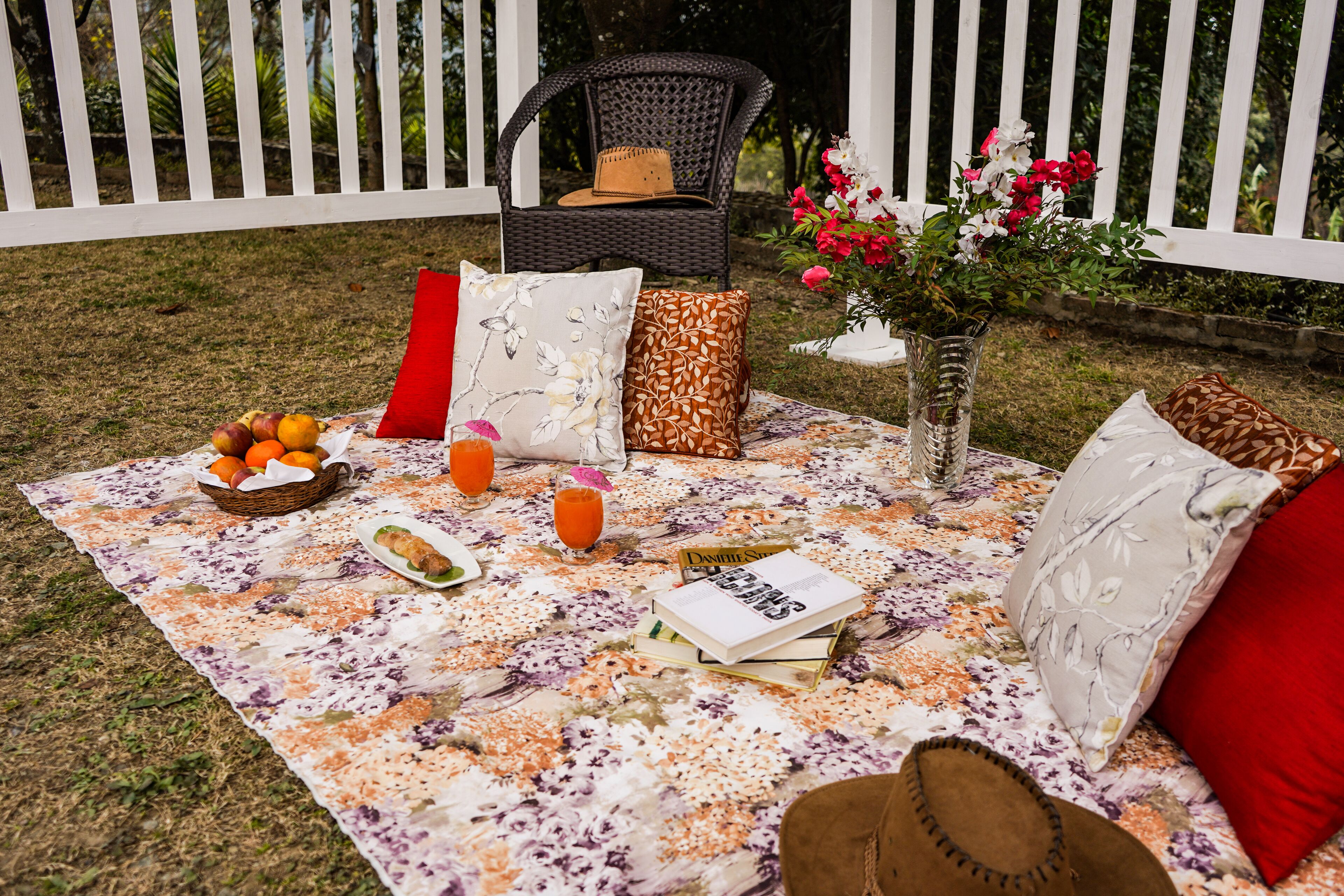 Montaje para un picnic al aire libre con una manta, comida, bebidas, un libro y una silla de mimbre.