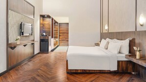 Una camera d'albergo moderna con pavimento in legno, un letto con biancheria bianca, una TV fissata al muro e un armadio in legno.