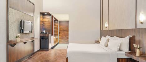 Una habitación de hotel moderna con piso de madera, cama con ropa blanca, televisor montado en la pared y armario de madera.