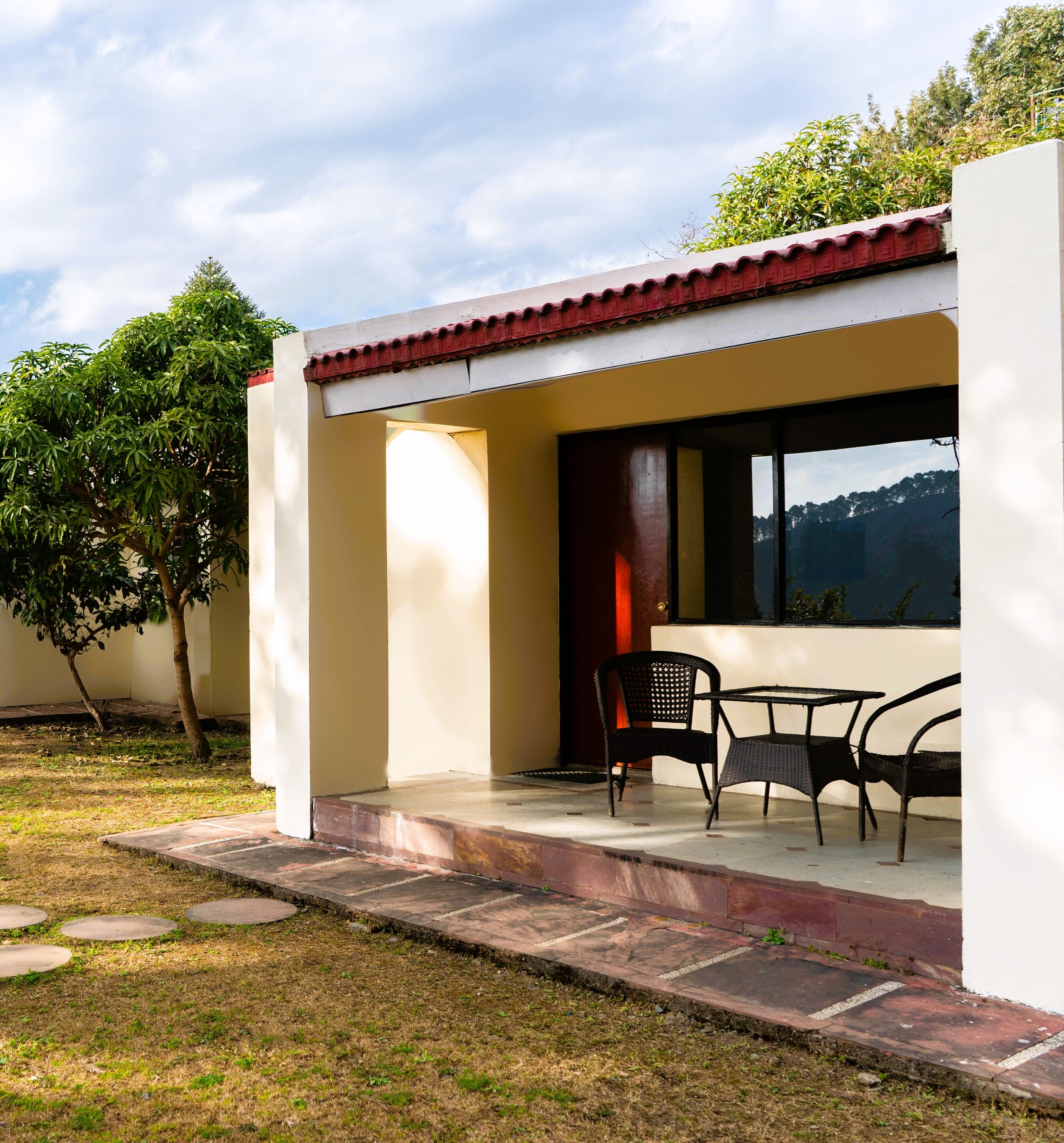 A patio area with a table and chairs, a red-tiled roof, and a view of trees and hills.