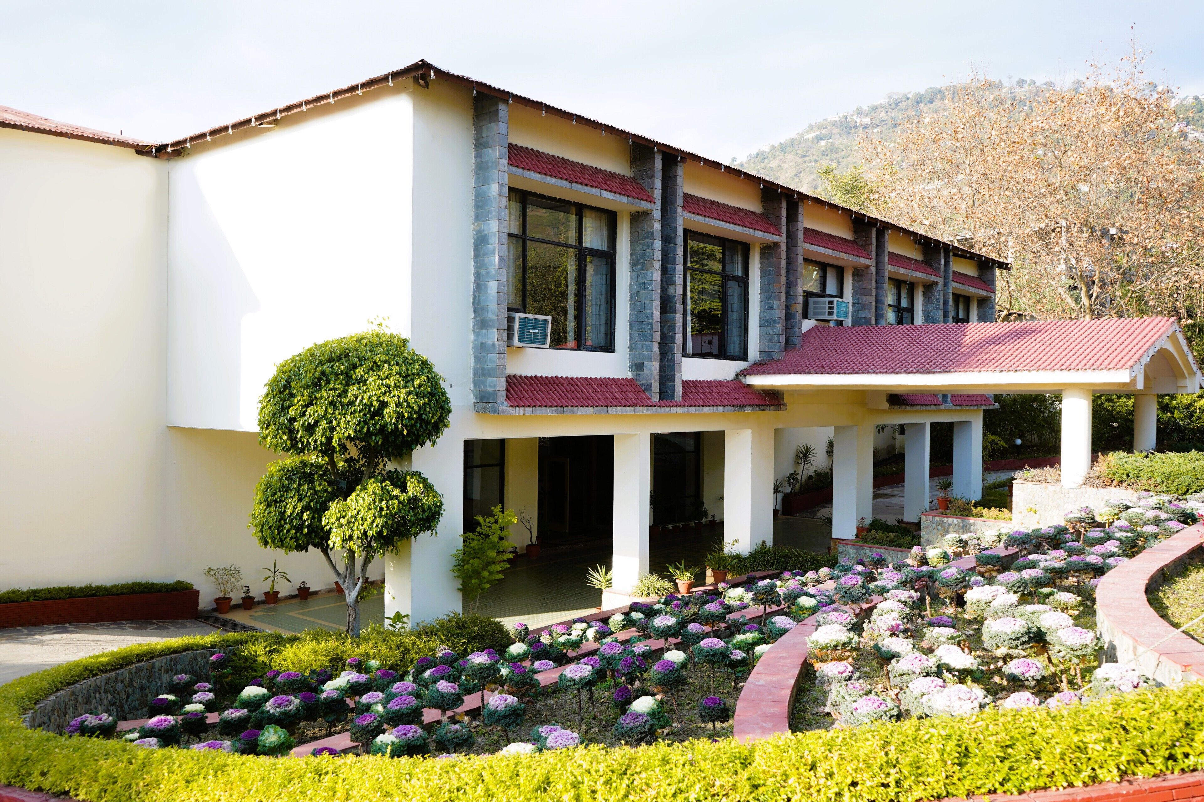 A building with a white facade, red roof, and a garden with various plants and flowers.
