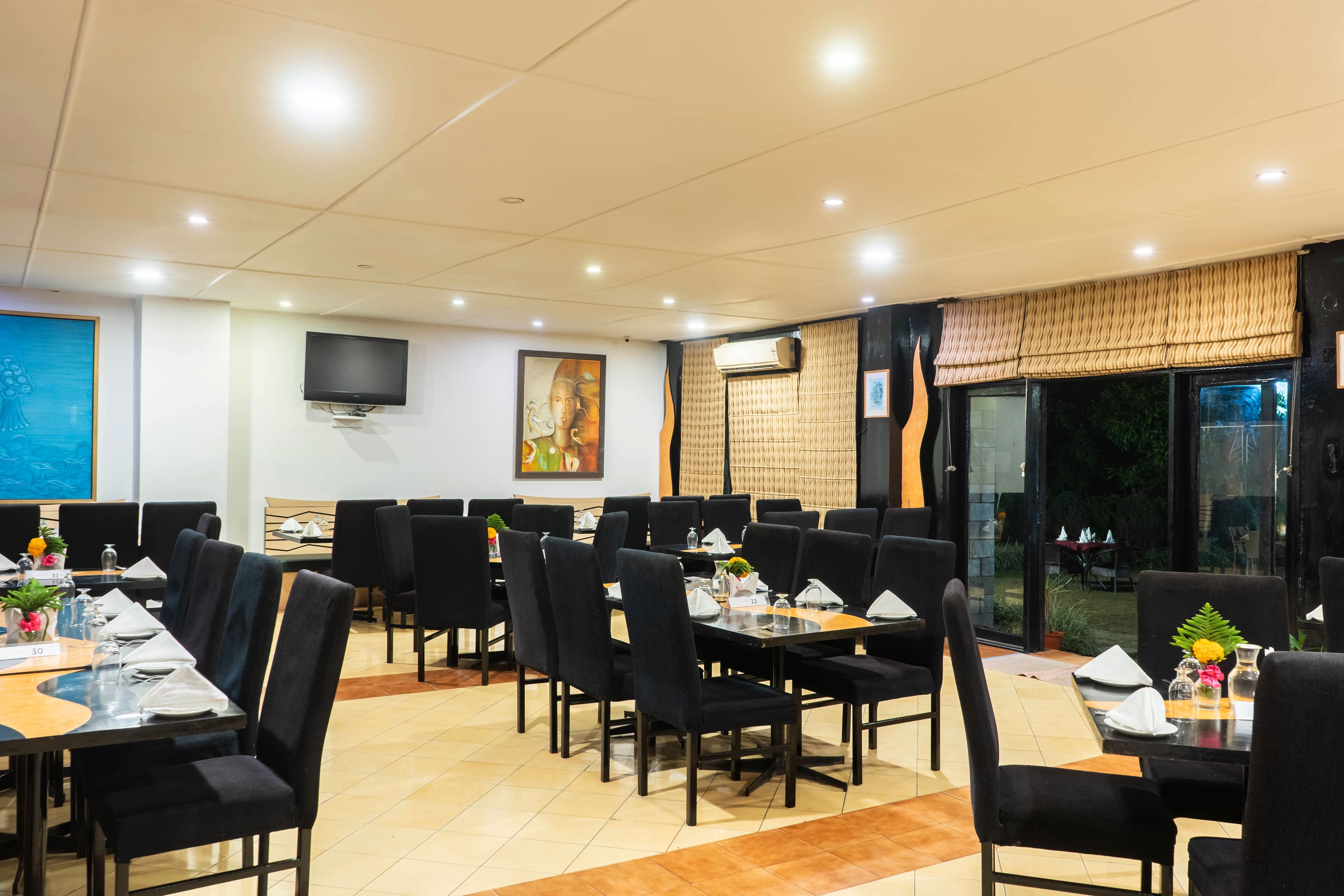 A restaurant with multiple tables and chairs, a flat-screen TV mounted on the wall, and a large window with a view of the outdoors.