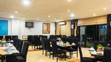 A restaurant with multiple tables and chairs, a flat-screen TV mounted on the wall, and a large window with a view of the outdoors.