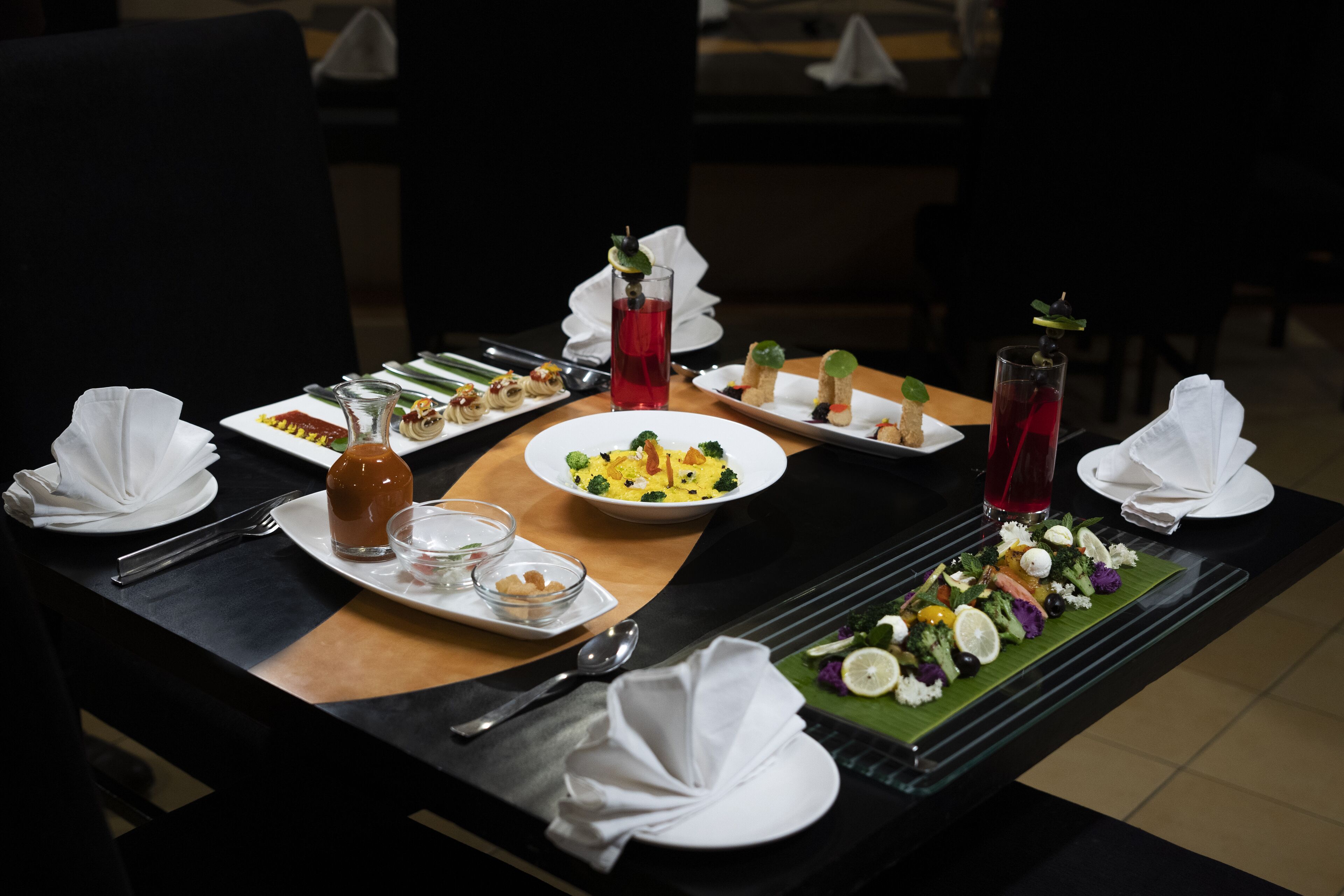 Una mesa de comedor dispuesta con varios platos, incluyendo un plato de verduras, un tazón de sopa y un vaso de bebida roja.