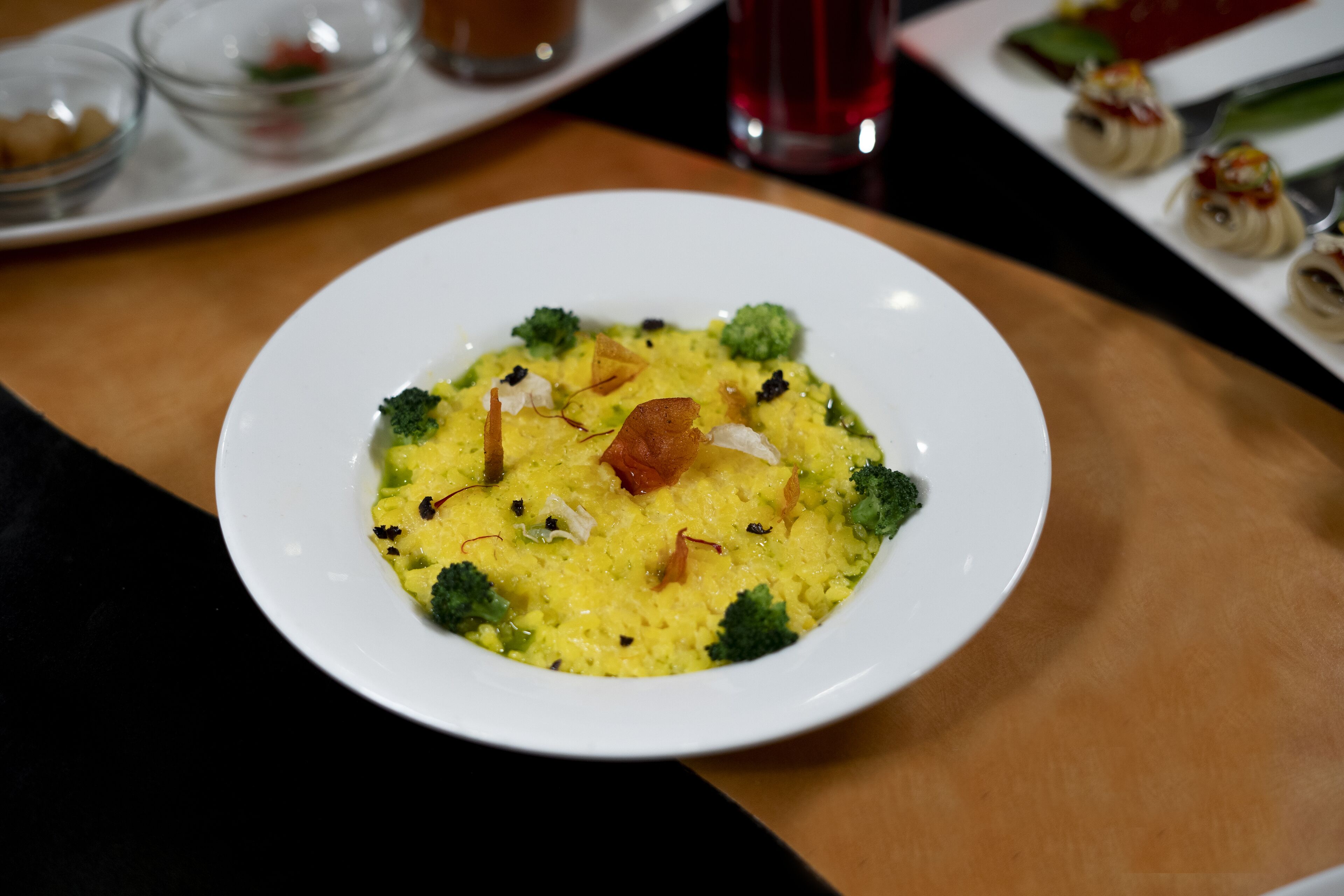 A white plate with a yellow dish, broccoli, and other garnishes on a wooden table.