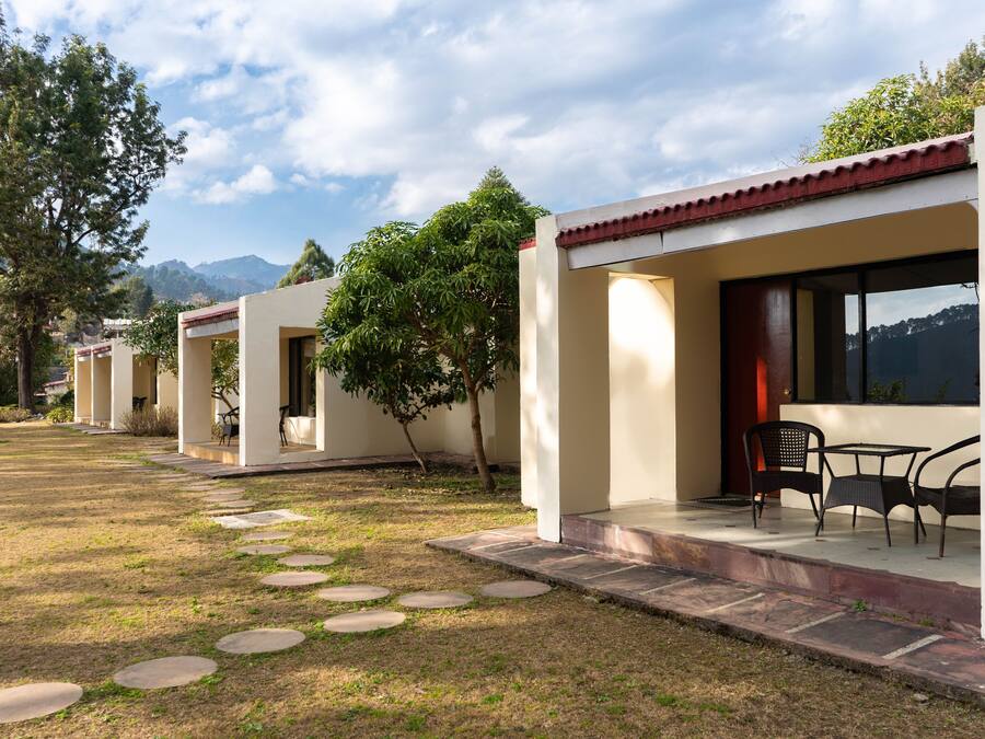 A row of modern, single-story buildings with a flat roof and a red-tiled roof edge. Each building has a covered patio with outdoor seating.