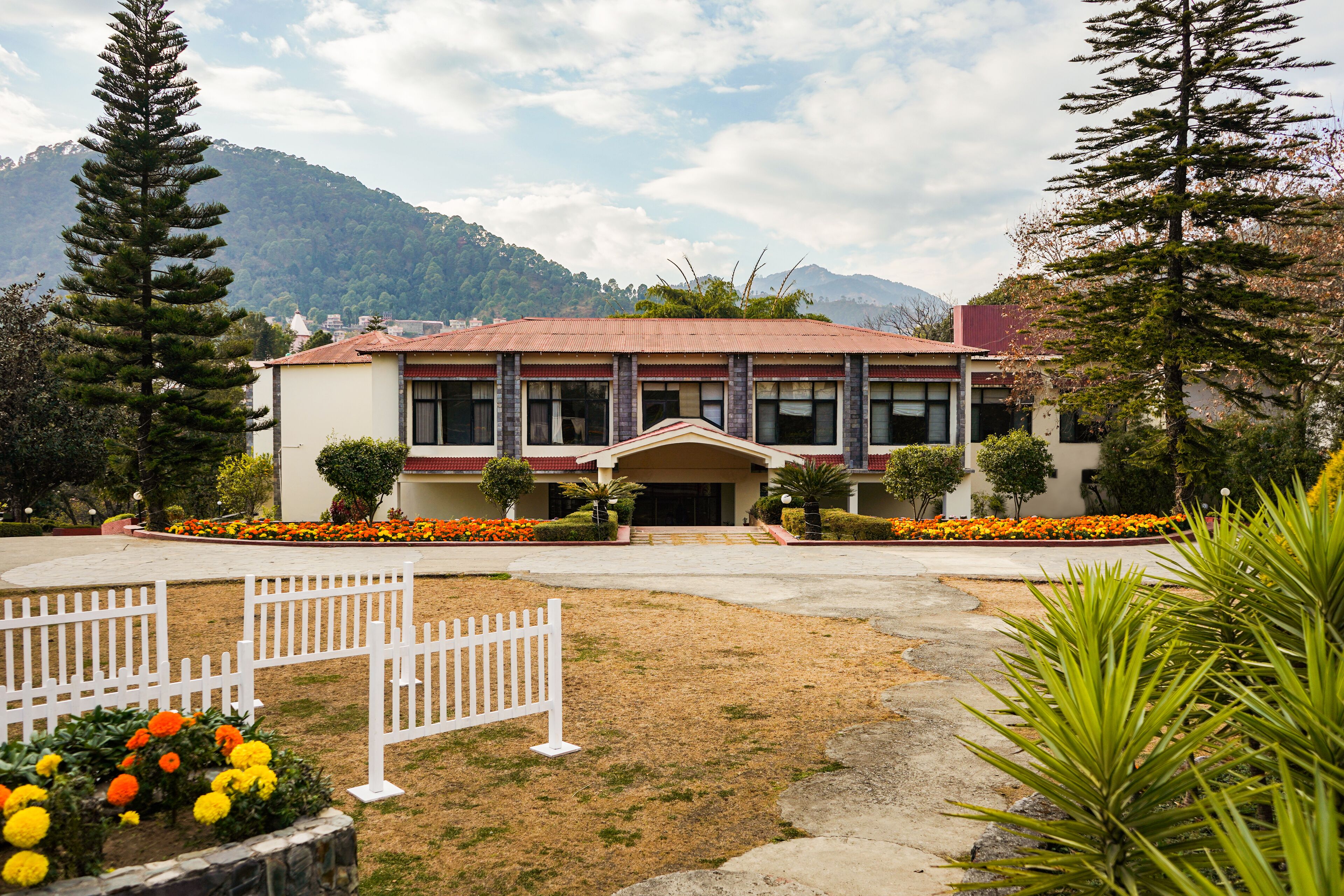 A building with a red roof, surrounded by a white fence, and a garden with orange flowers.