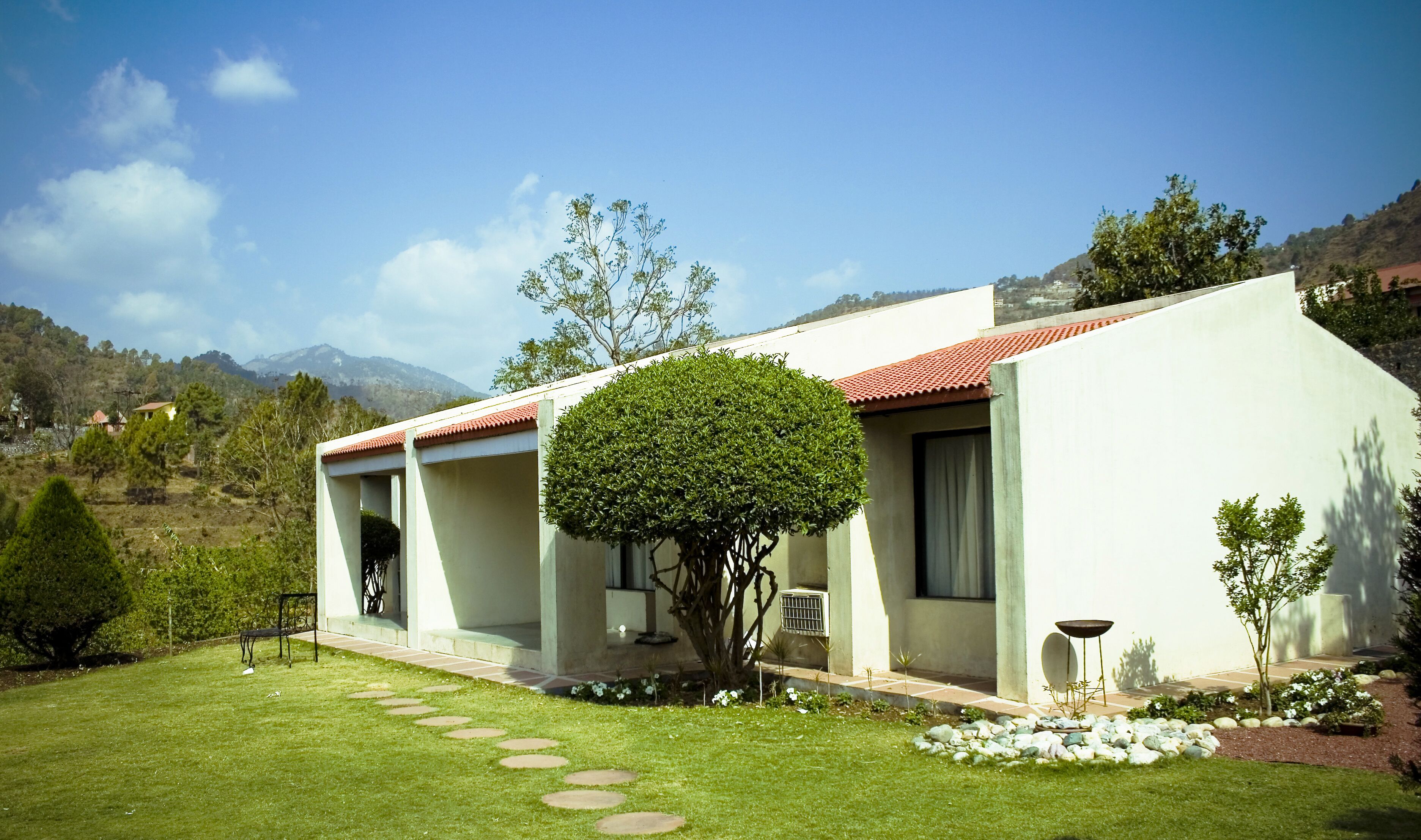 Una casa moderna con techo de tejas rojas, un césped bien cuidado y un camino de piedra que conduce a la entrada.
