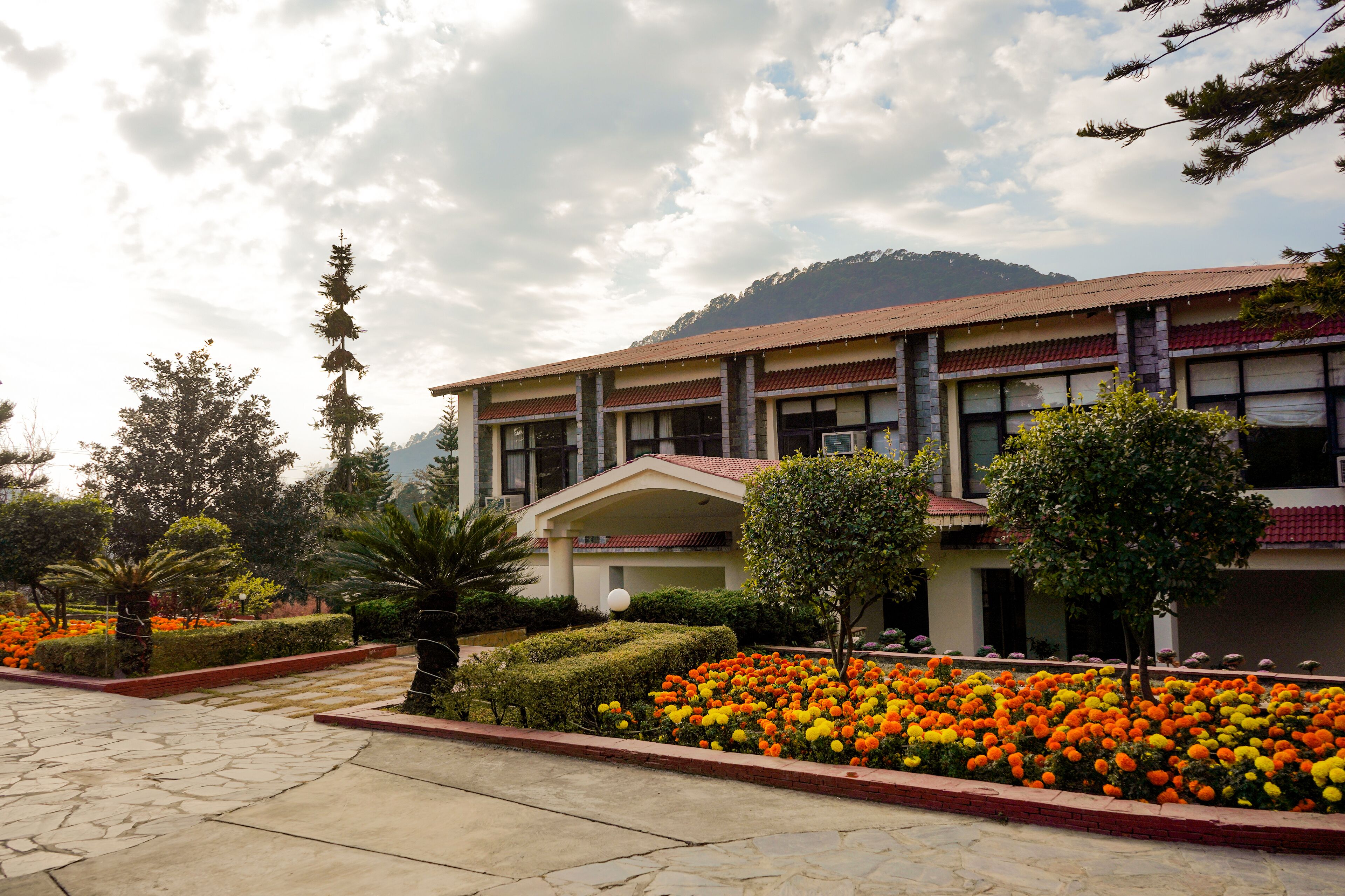 A building with a tiled roof and multiple windows, surrounded by well-maintained gardens with various plants and flowers.