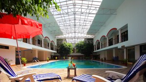 Una piscina interna con sedie a sdraio e un tavolo con bevande, circondata da piante in vaso e un soffitto in vetro.