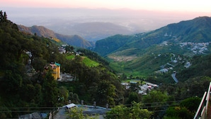 A mountainous landscape with terraced fields, a few scattered buildings, and a prominent yellow structure on a hill. - Country Inn (Dehradun)
