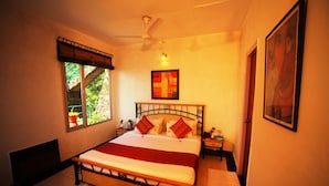 A bedroom with a bed, a nightstand, a window with a view of greenery, and a ceiling fan. - Country Inn (Dehradun)