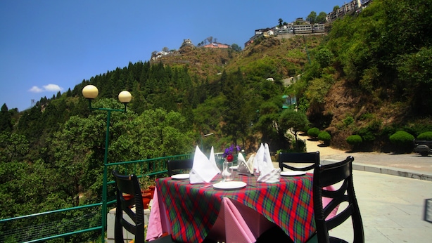 A table set outdoors with a view of a hillside and buildings. - Country Inn (Dehradun)