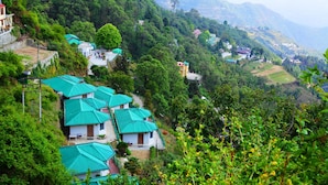A hillside village with traditional houses, terraced fields, and a prominent tower. - Country Inn (Dehradun)