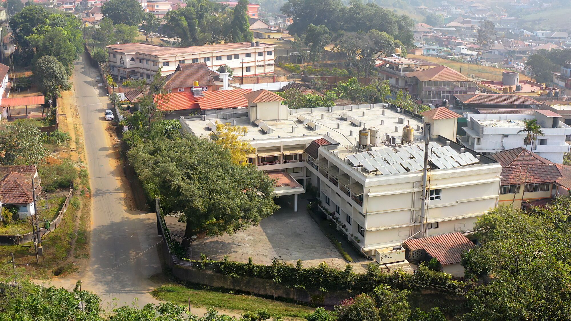 A multi-story building with a flat roof, surrounded by residential houses with red-tiled roofs.